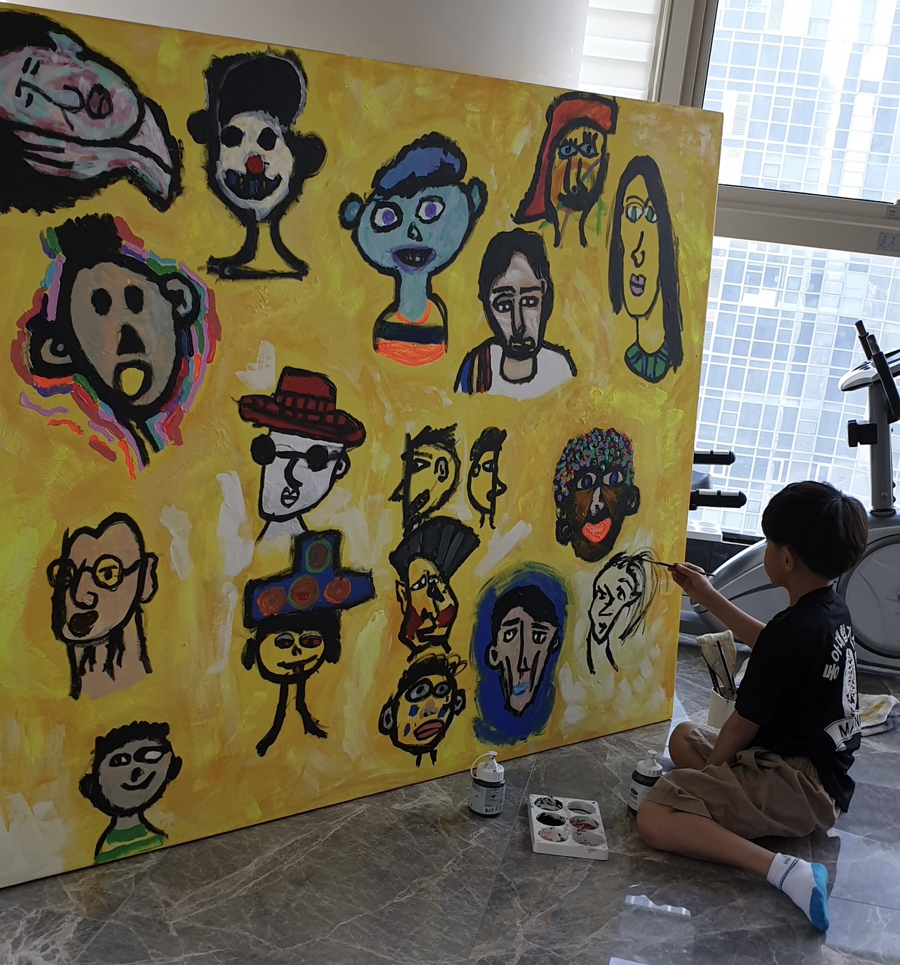 Boy painting faces on a large yellow canvas.